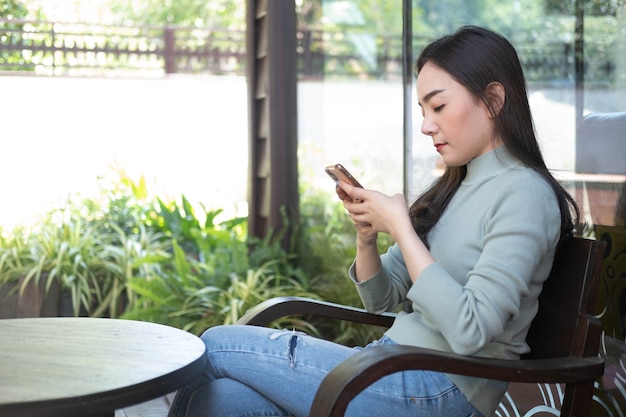 コーヒーショップでスマートフォンを使用して笑顔の若いアジアの女性オンライン技術システムの概念を動作させる