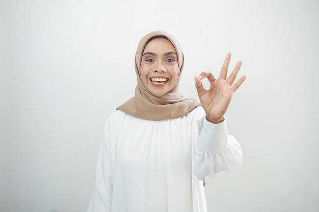 Smiling young Asian woman in white casual showing okay gesture isolated over white background