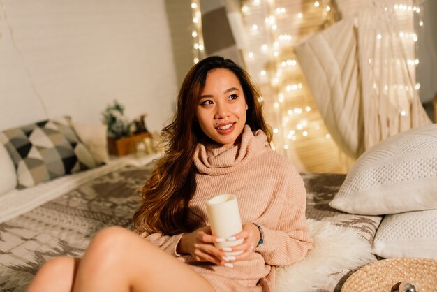 Smiling young asian woman with christmas present box near christmas tree