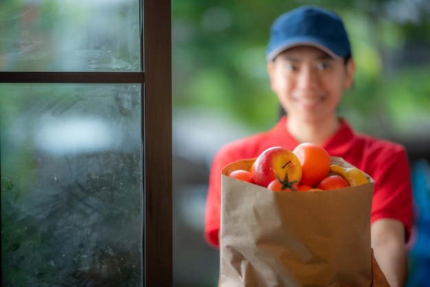 Una sorridente giovane donna asiatica consegna merci davanti alla porta di casa, concetto di vendita al dettaglio online, consegna veloce, concetto di stile di vita urbano, servizio di acquisto online, trasporto.