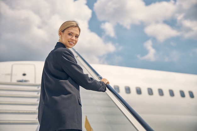 Smiling young attractive blonde modern airport worker holding on to the handrail on the stairs