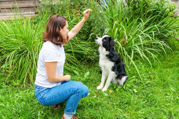 Smiling young attractive woman playing with cute puppy dog border collie in garden