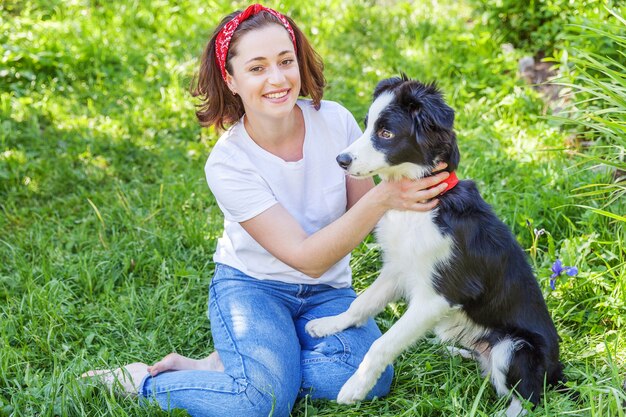 Smiling young attractive woman playing with cute puppy dog border collie in summer garden or city park outdoor background.