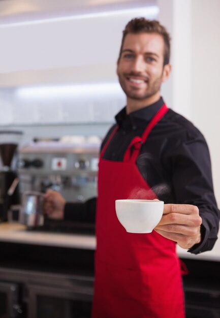 Smiling young barista holding jug and cup of coffee