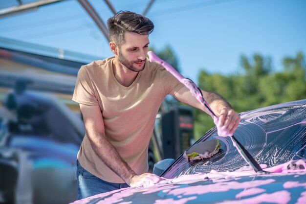 Smiling young bearded man washing windshield wiper