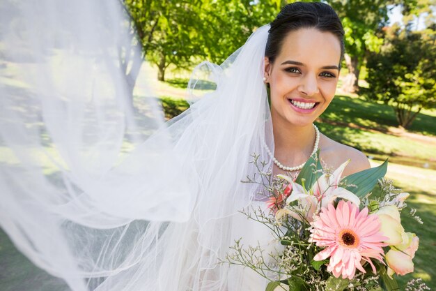 Smiling young beautiful bride with bouquet in park