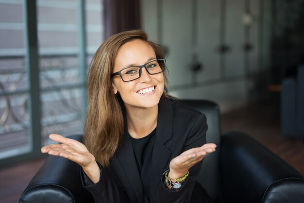 smiling young beautiful brown-haired woman looking at camera, raising open hands