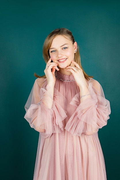 Sorridente giovane bella ragazza in un vestito rosa su sfondo verde colore di sfondo verde con copia spazio guarda nella fotocamera