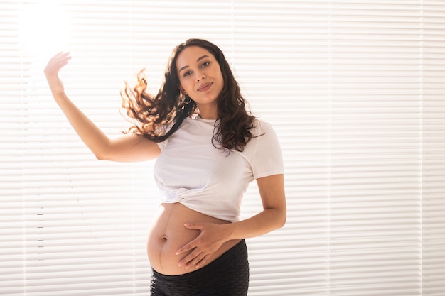 Smiling young beautiful pregnant woman touching her belly and hair and rejoicing concept of health