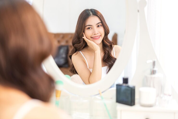 若い美しいきれいなアジアの女性の笑顔は、ミラーを見てきれいな新鮮な健康的な白い肌です。アジアの女の子は手で彼女の顔に触れて、home.spaと美しさの概念でクリームを適用します。