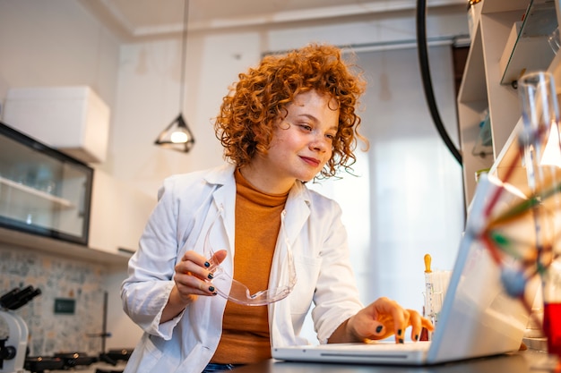 Smiling young biochemist using laptop at her desk in laboratory.