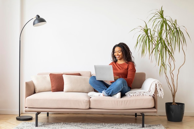 노트북으로 집에서 일하는 미소 짓는 젊은 흑인 프리랜서 여성