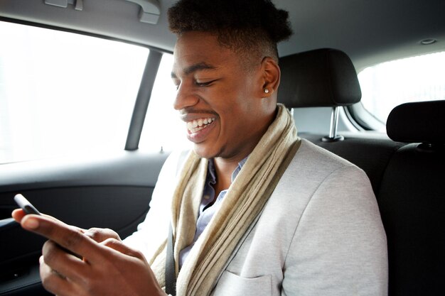 smiling young black man looking at cellphone while in backseat of car