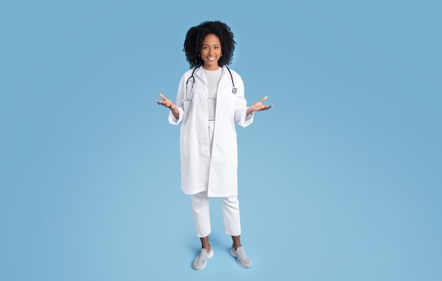 흰색 코트에 웃는 젊은 흑인 여성 의사 치료사는 손에 복사 공간을 잡고