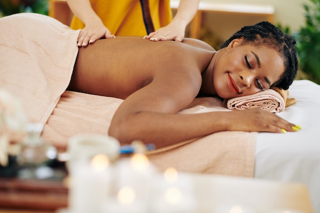 Photo smiling young black woman enjoying relaxing back massage in beauty salon