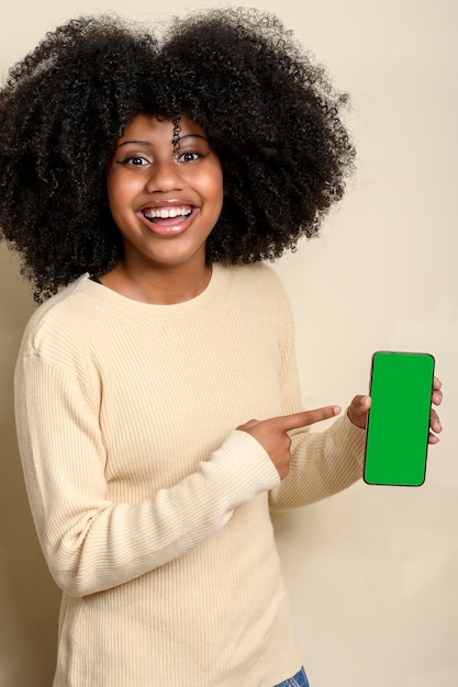 Smiling young black woman points at her cell phone screen cell phone screen in green color for crop