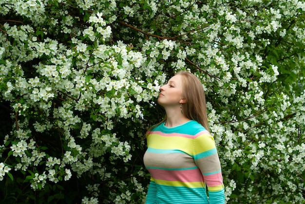 リンゴの木の花の香りを楽しんで笑顔の若いブロンドの女性