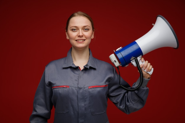 Smiling young blonde female engineer wearing uniform holding speaker 