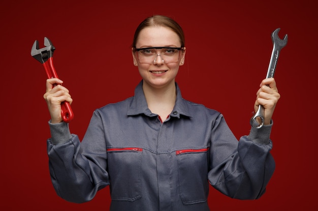 Sorridente giovane bionda ingegnere femminile indossa uniformi e occhiali di sicurezza che tengono le chiavi