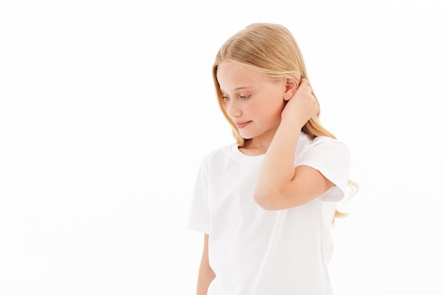 Smiling young blonde girl in casual clothes touching her hair and looking away on white