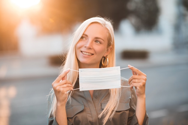 Smiling young blonde girl holding medical protective mask