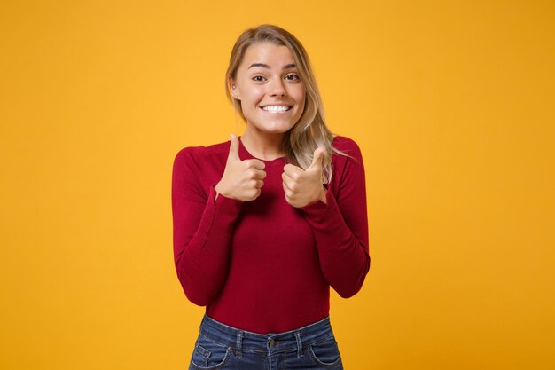 Foto sorridente giovane donna bionda ragazza in abbigliamento casual in posa isolato sul ritratto in studio di sfondo parete giallo arancio. concetto di stile di vita di emozioni sincere della gente. simula lo spazio della copia. mostrando i pollici in su.