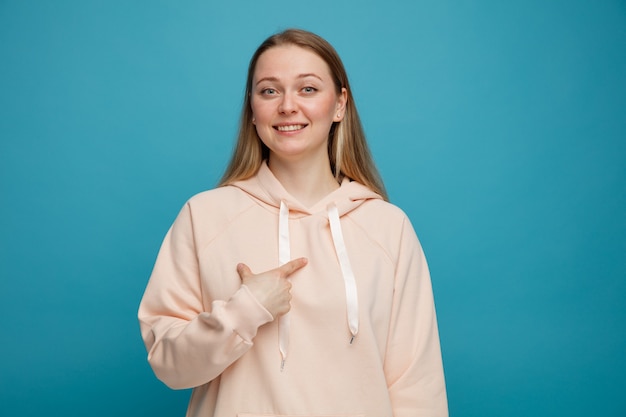 Smiling young blonde woman pointing at herself 