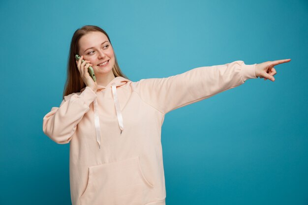 笑顔の若いブロンドの女性が電話で話しているのを見て、横を指しています