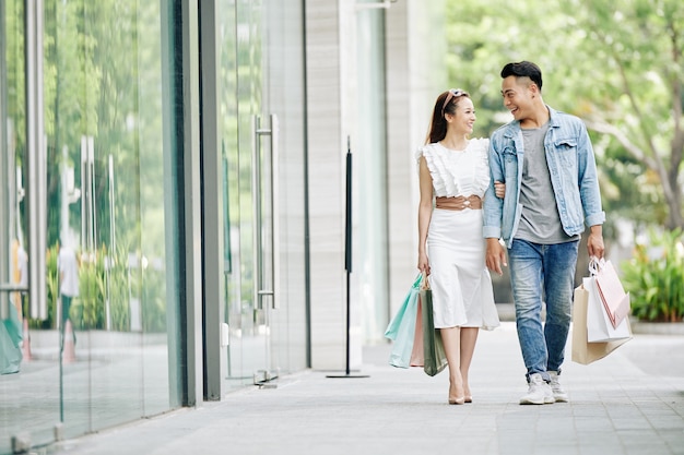 Smiling young boyfriend and girlfriend with shopping bags walking in the street with shopping bags