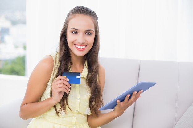 Smiling young brunette holding credit card and tablet