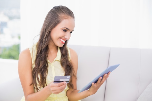 Smiling young brunette looking at tablet and credit card