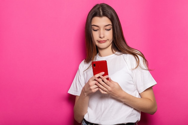 Smiling young brunette woman girl posing isolated on pastel pink wall background studio portait. People lifestyle concept. Mock up copy space. Using mobile phone, typing sms message