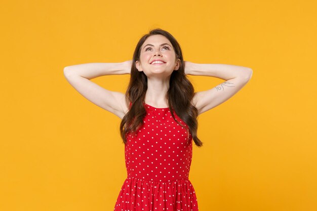 Smiling young brunette woman girl in red summer dress posing isolated on yellow background studio po