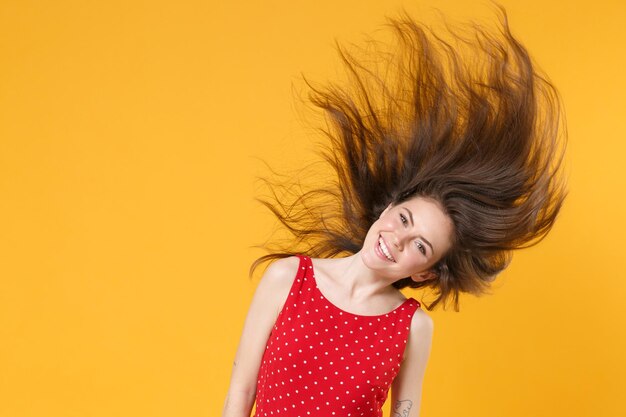 Smiling young brunette woman girl in red summer dress posing isolated on yellow wall background stud