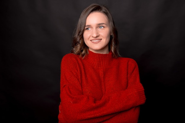 Smiling young brunette woman girl in red sweater posing isolated on dark background studio portrait.