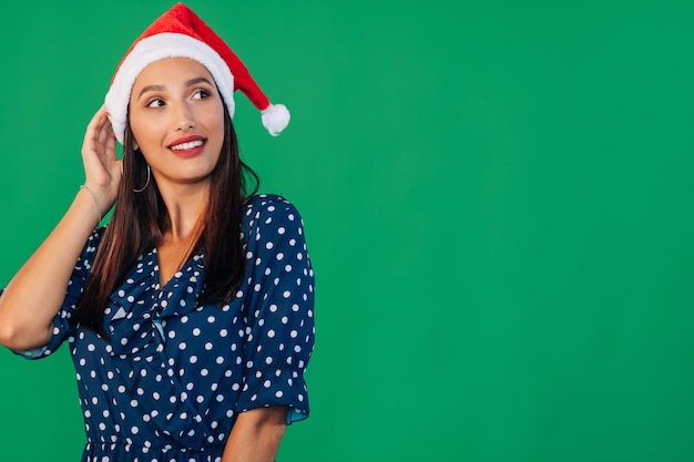 Smiling young brunette woman in santa hat posing isolated on green background studio portrait People sincere emotions lifestyle concept