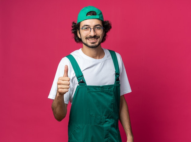 Улыбающийся молодой человек-строитель в униформе с кепкой, показывая большой палец вверх