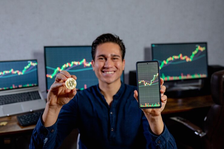 ビットコインコインとスマートフォンを持って笑顔の若いビジネスマンが通貨価値の成長とともにグラフを表示します。