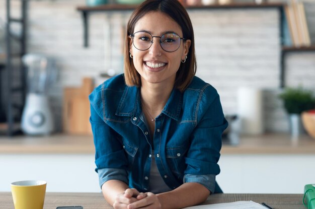 写真 自宅のキッチンでカメラを見て笑顔の若いビジネス女性