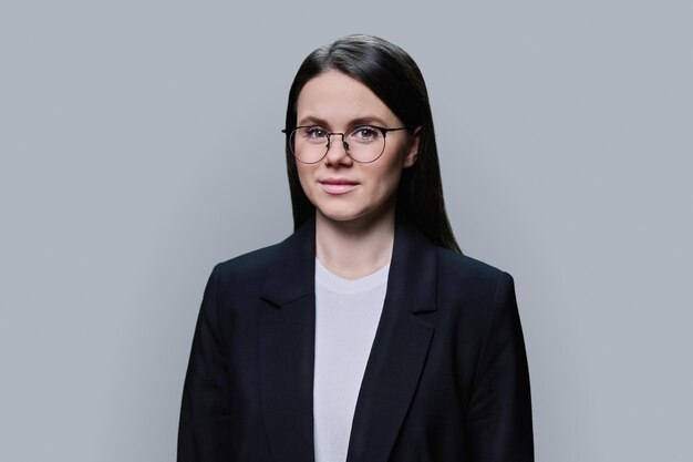 Smiling young business woman looking at camera on grey background