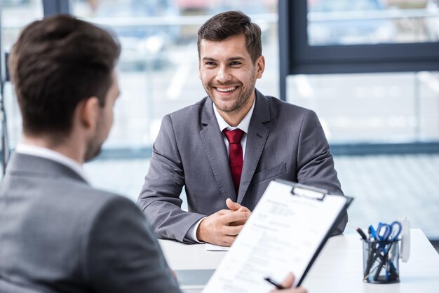 Smiling young businessman looking at manager with clipboard at job interview, business concept