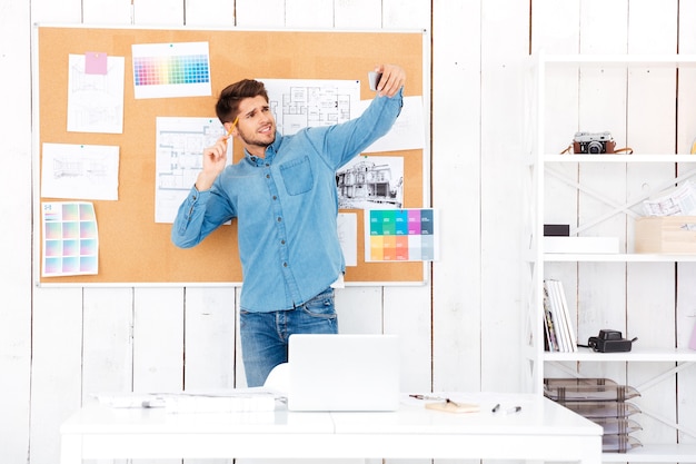 Smiling young businessman making selfie while standing in front of office board