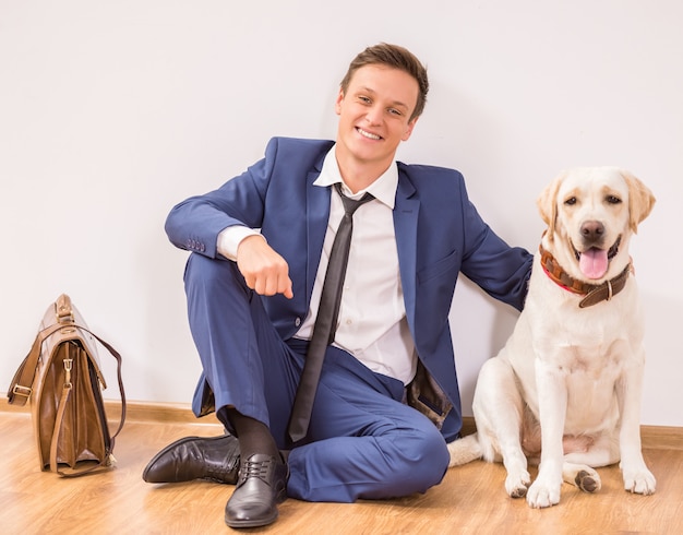 Giovane uomo d'affari sorridente con il suo cane che si siede sul pavimento.