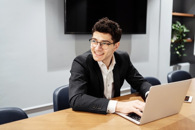 Smiling young businessman working on a laptop at a modern conference table displaying