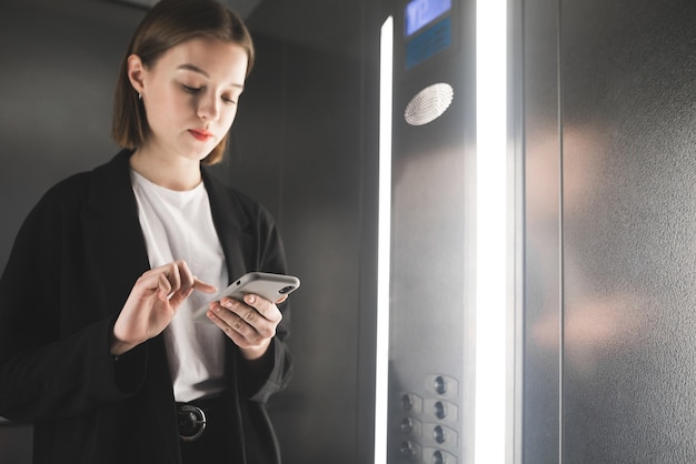 Smiling young businesswoman is writing messages on her mobile phone in the lift.