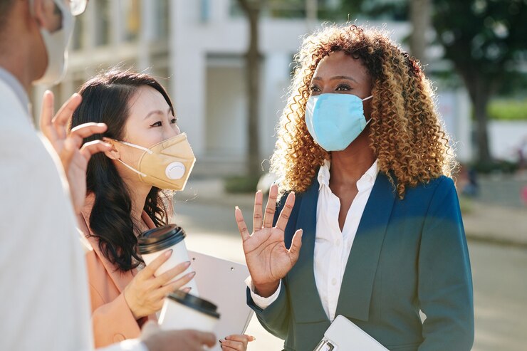 Photo smiling young businesswoman in protective mask talking to colleagues when having outdoor meeting
