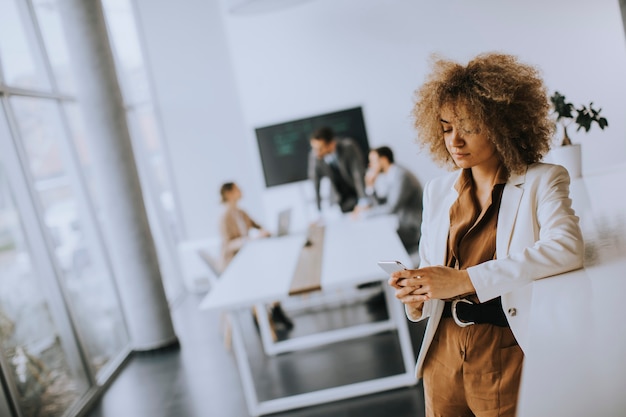 Smiling young businesswoman using mobile phone in modern office