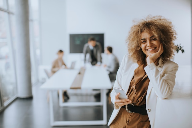 Smiling young businesswoman using mobile phone in modern office