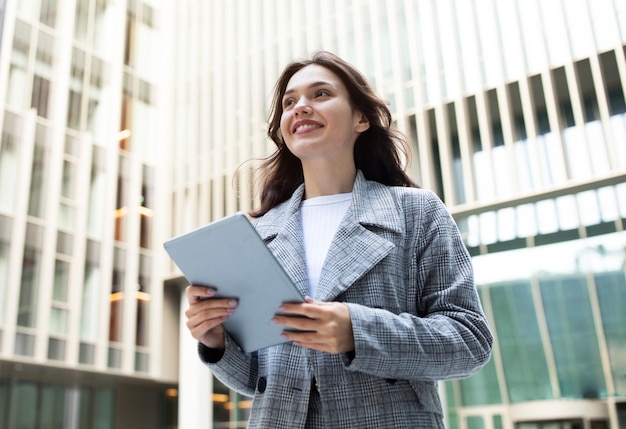 Smiling young businesswoman with digital tablet posing in urban area