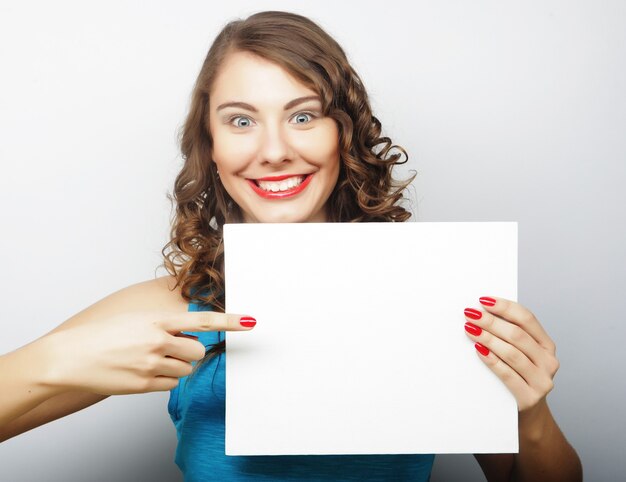 Smiling young casual style woman showing blank signboard, over grey background isolated